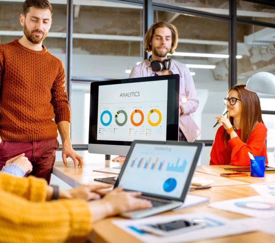 Group of young coworkers dressed casually working together on the computers with some charts sitting in the modern office interior